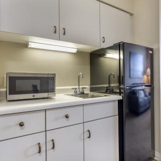A compact kitchen area with a microwave, refrigerator, sink, and white cabinets.