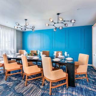 A modern conference room with blue walls, elegant chandeliers, and comfortable seating around a large table.