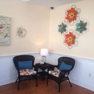 A cozy seating area with two wicker chairs, a small table, and colorful wall art.