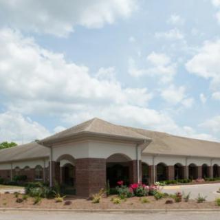 A large brick building with arched windows under a partly cloudy sky, surrounded by landscaping.
