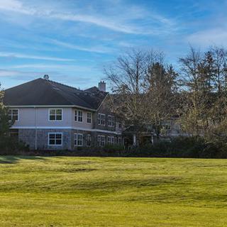 A suburban house with a large lawn and trees under a blue sky.