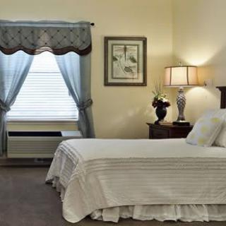 A cozy bedroom with a neatly made bed, decorative lamp, and window with curtains.