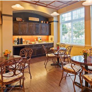 A cozy cafe interior with tables and chairs, warm lighting, and large windows.