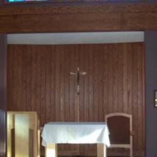 A small chapel with a wooden altar, a cross on the wall, and chairs for seating.