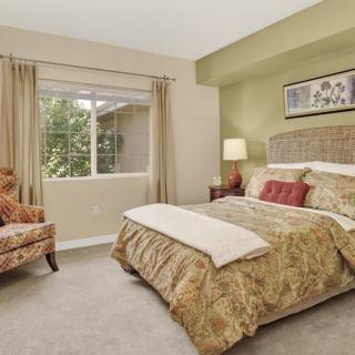 A cozy and well-decorated bedroom with a large bed, an armchair, and a window allowing natural light.