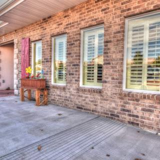 A brick house exterior with large windows, shutters, and a patio adorned with a flower box.