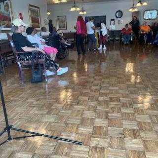 A community gathering taking place indoors, featuring a performance with attendees enjoying the event.