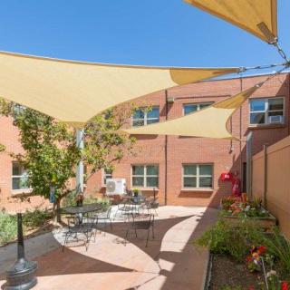 A sunny courtyard with shade sails, featuring outdoor seating next to a brick building.