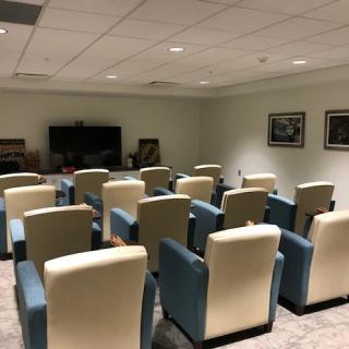 A small theater room with multiple rows of chairs facing a large screen.