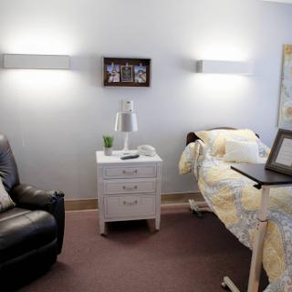 A cozy room featuring a bed, nightstand with a lamp, and a comfortable chair.