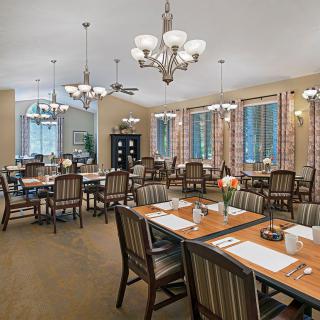 A well-lit dining room with neatly arranged tables and chairs, featuring elegant chandeliers.