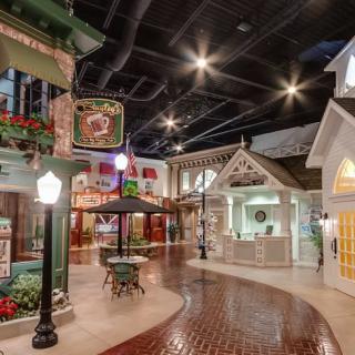An indoor village setting with charming shops and cobblestone walkways, illuminated by street lamps.