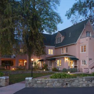 A charming house exterior lit up in the evening, surrounded by trees.