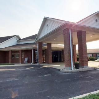 A brick building with a covered entrance and driveway, illuminated by sunlight.