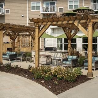 A cozy outdoor patio area with pergolas, seating, and landscaping at an apartment complex.