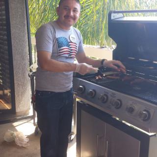 A person smiling while grilling on a patio during the day.