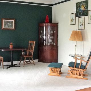 A cozy living room with wooden furniture, a table and chairs, a glass cabinet, a floor lamp, and decorative wall art.