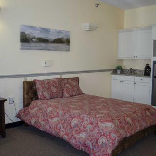 A cozy bedroom with a kitchenette featuring a patterned bedspread and wall art.