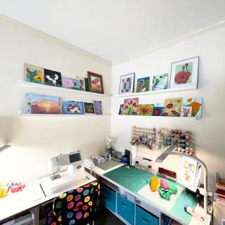 A well-organized craft room featuring colorful paintings on shelves, a sewing machine, and various art supplies.