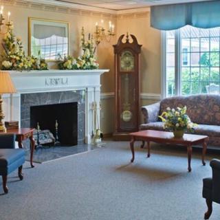 A traditional living room featuring a fireplace, grandfather clock, and comfortable seating with floral decorations.
