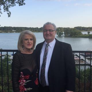 A happy couple posing together by the lake, dressed in formal attire.