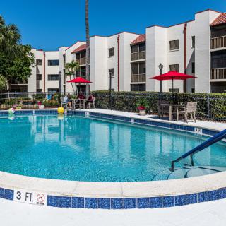 An inviting swimming pool at a residential apartment complex, surrounded by lounge chairs and red umbrellas.