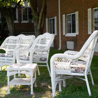 Wicker chairs and a table set on a lawn outside a brick building.
