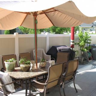 A cozy patio setup with a large umbrella over a table and chairs, surrounded by potted plants.