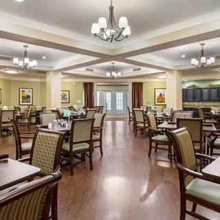 A spacious and elegantly decorated dining room with multiple tables and chairs, featuring chandeliers and wooden flooring.