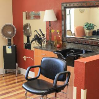 A cozy hair salon setup featuring a black barber chair, a large mirror, and various hairdressing tools.