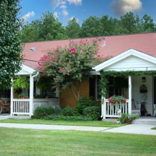 A charming cottage with a porch surrounded by a lush garden and well-maintained lawn.