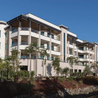 A modern apartment building with balconies surrounded by trees under a clear blue sky.