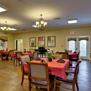 A cozy dining room setup with tables covered in red tablecloths and elegant chandeliers overhead.