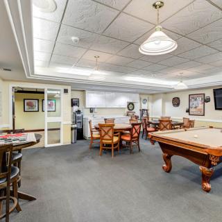 A spacious game room featuring a pool table, ample seating, and indoor lighting, decorated with various wall hangings.
