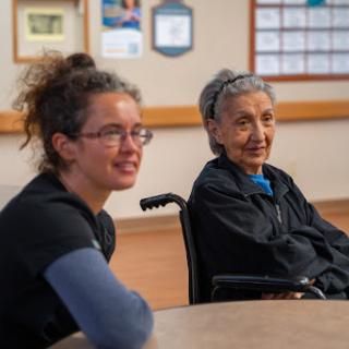 A young woman and an elderly woman engage in conversation at a community center.