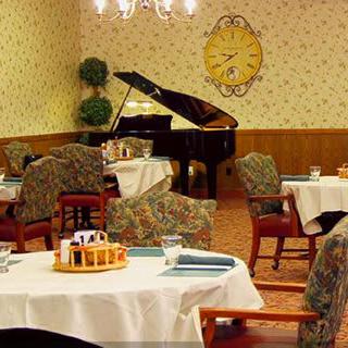 A cozy dining room with elegantly set tables, a grand piano in the background, and warm, inviting decor.