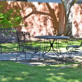 A scenic outdoor setting with iron chairs and a table casting shadows on the grass.