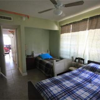 A cozy bedroom with a plaid-covered bed, ceiling fan, and large window with curtains.