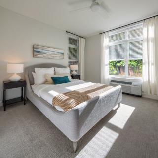 A bright and modern bedroom with minimalist decor, featuring a bed by large windows letting in natural light.