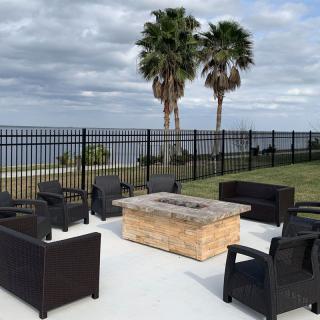 An outdoor seating area with a fire pit overlooking the ocean, surrounded by palm trees and a fence.