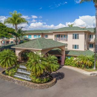 A tropical residential building with a fountain at the entrance surrounded by lush palm trees.