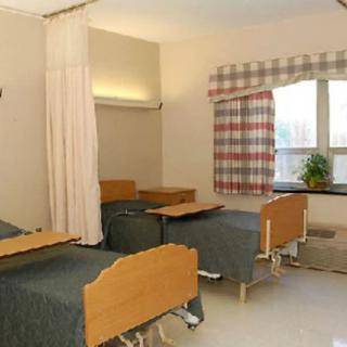 A hospital room with two beds, bedside tables, and a window with curtains.