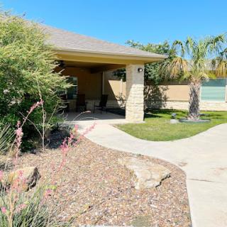 A serene residential front yard featuring a pathway, lush greenery, and palm trees under a clear blue sky.
