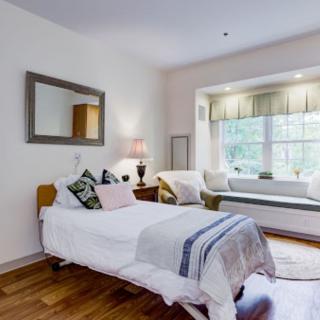 A cozy bedroom with a single bed, decorative pillows, and a window seat.
