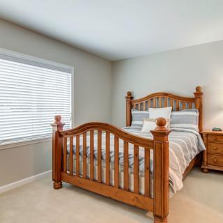 A cozy bedroom with a wooden bed frame and striped bedding next to a window with blinds.