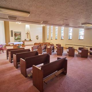 A serene chapel interior with rows of wooden pews and an altar at the front.
