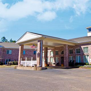 The image shows the exterior of a hotel building with a covered entrance on a sunny day.