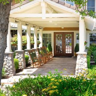 A charming front porch with rocking chairs and stone pillars, surrounded by lush landscaping.