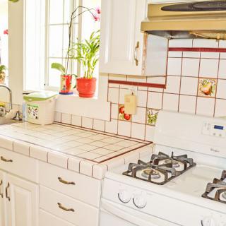 A bright kitchen with tiled surfaces, a stove, and potted plants by the window.