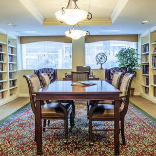 A cozy library room with a wooden table and chairs surrounded by bookshelves.